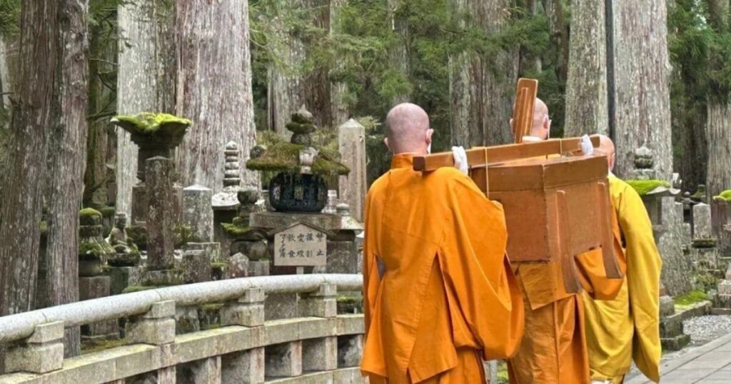 高野山僧侶穿著袈裟，背負木箱，走在佈滿苔蘚的奧之院石道上