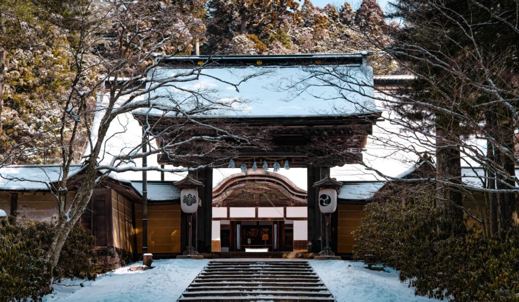 冬季高野山寺院入口，覆蓋白雪的屋頂與庭院景色，展現靜謐莊嚴的氛圍。